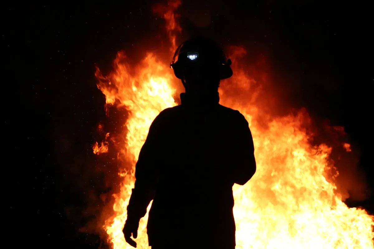 A firefighter silhouetted against flames at night