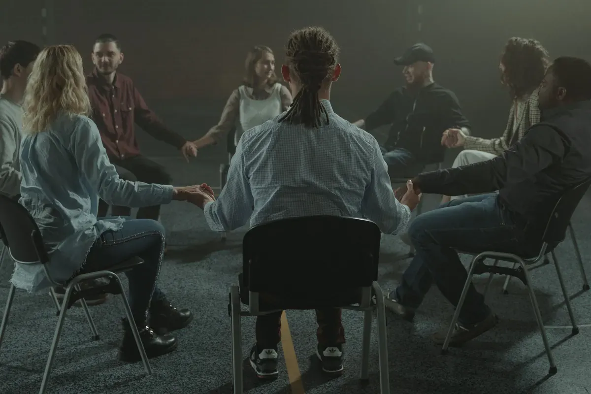 A small support group seated in a circle in a dim room, seen from behind