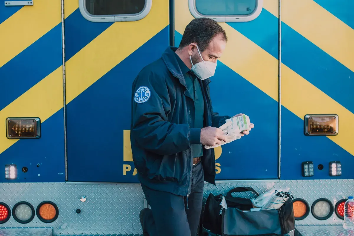 A paramedic standing alone at the back of an ambulance, looking down