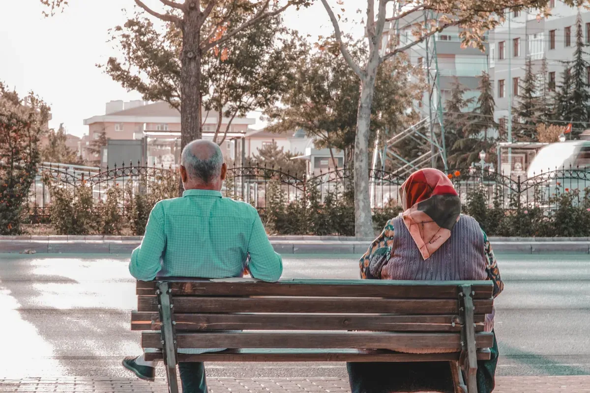 Two people seen from behind sitting on a park bench