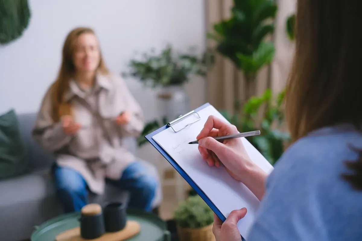 A counsellor taking notes on a clipboard while a client talks