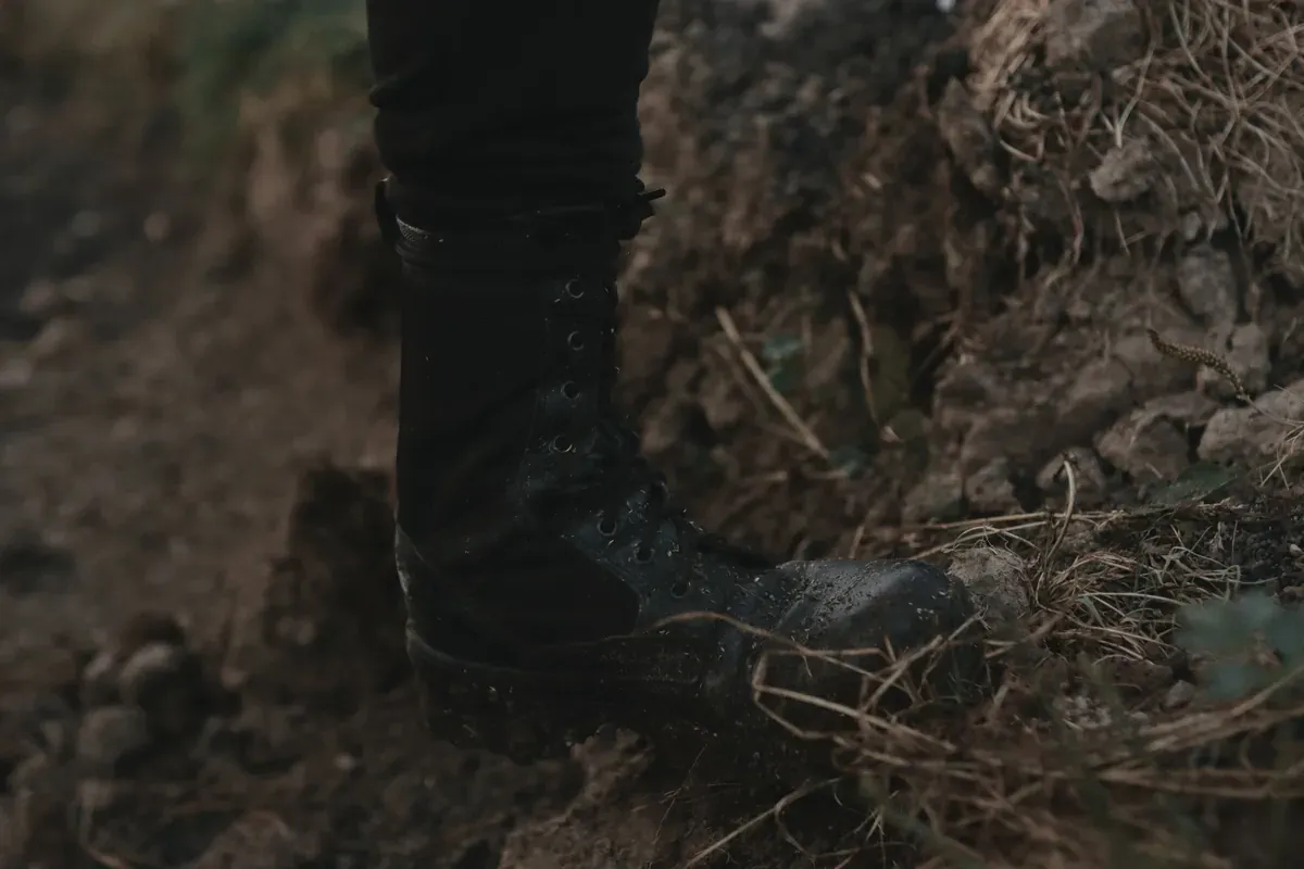 A black work boot stepping onto rough, muddy ground