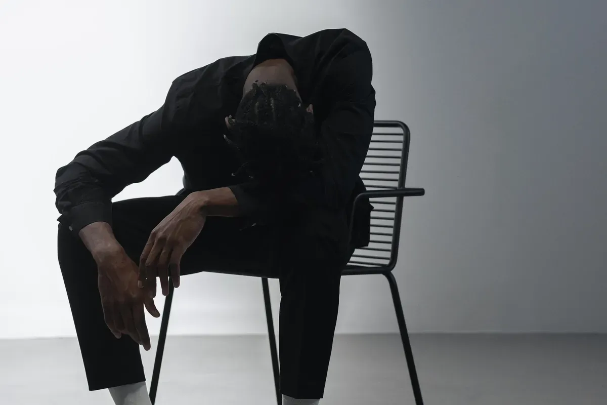 A man sitting on a chair with his head bowed onto his arm